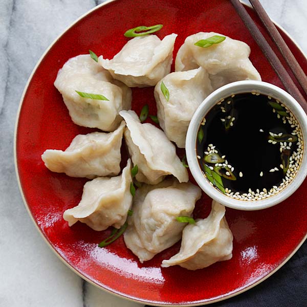 Pork and chives dumplings served on a red plate with dipping sauce. 