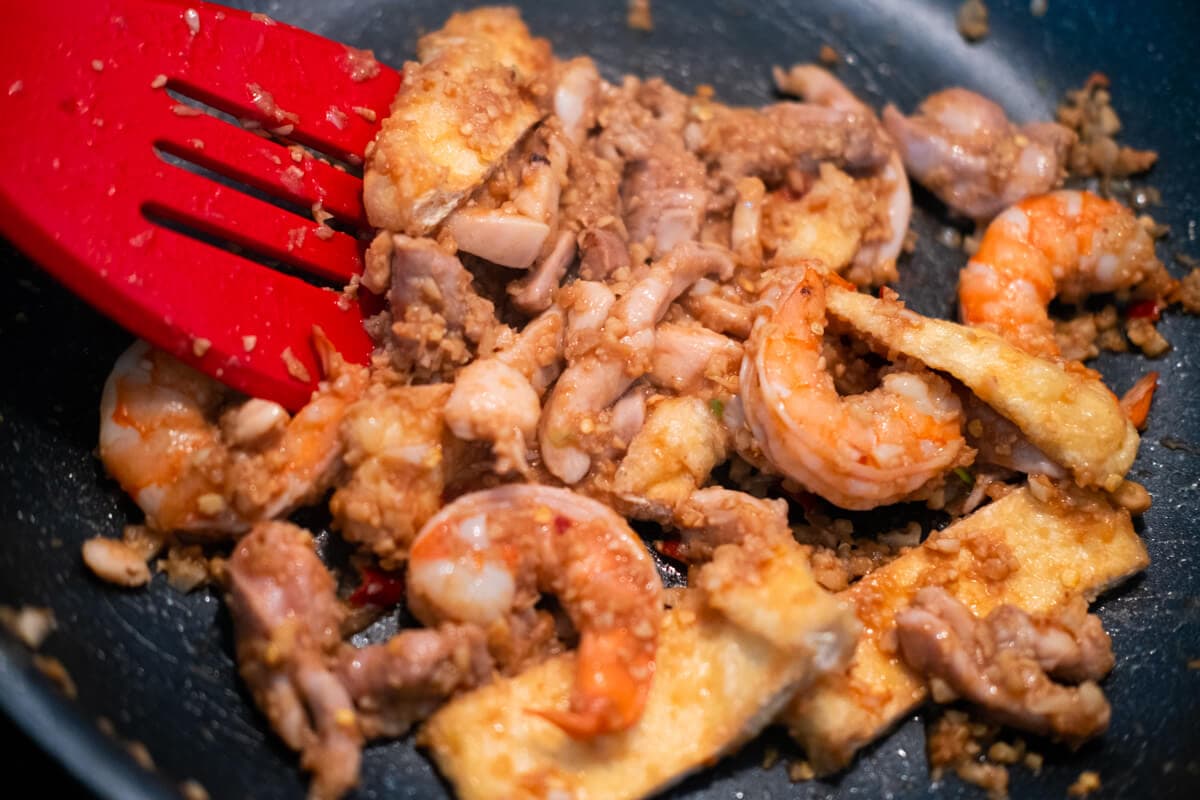 Stir frying shrimp, tofu, spice paste and fermented yellow bean sauce in a wok. 