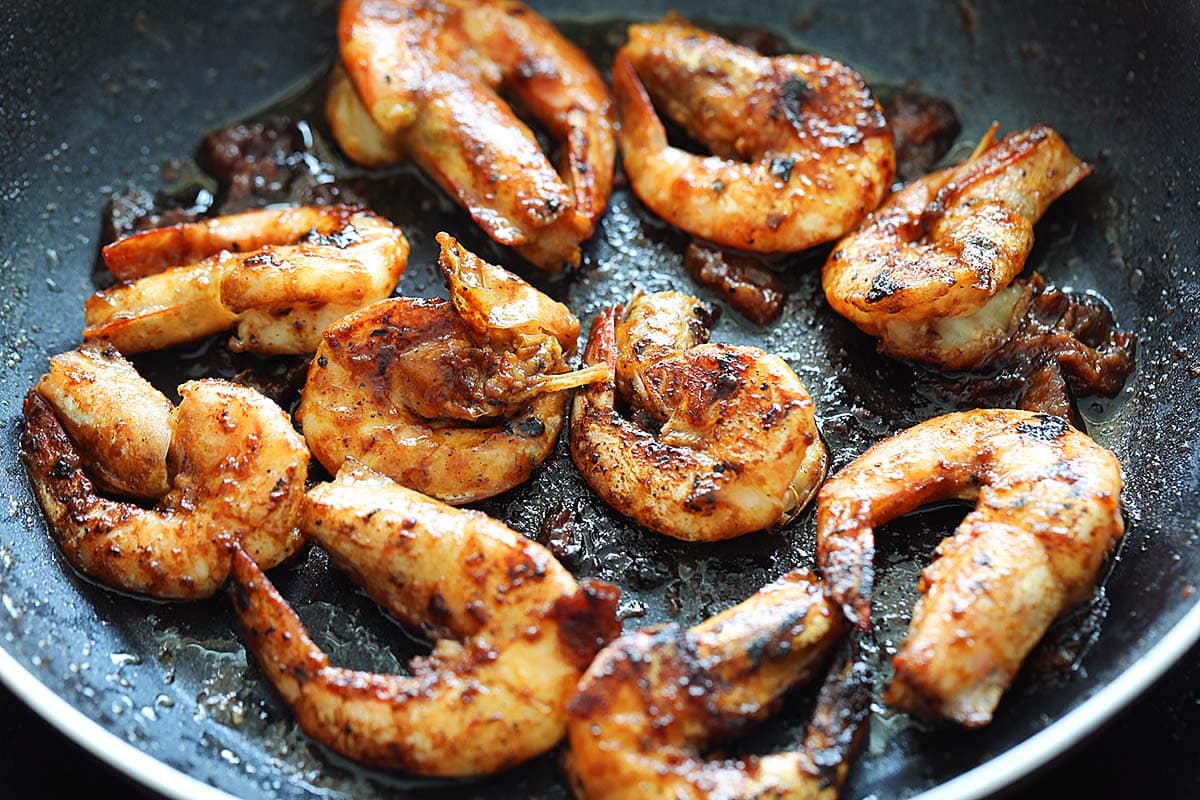 Cooking asam tamarind prawns in a skillet.