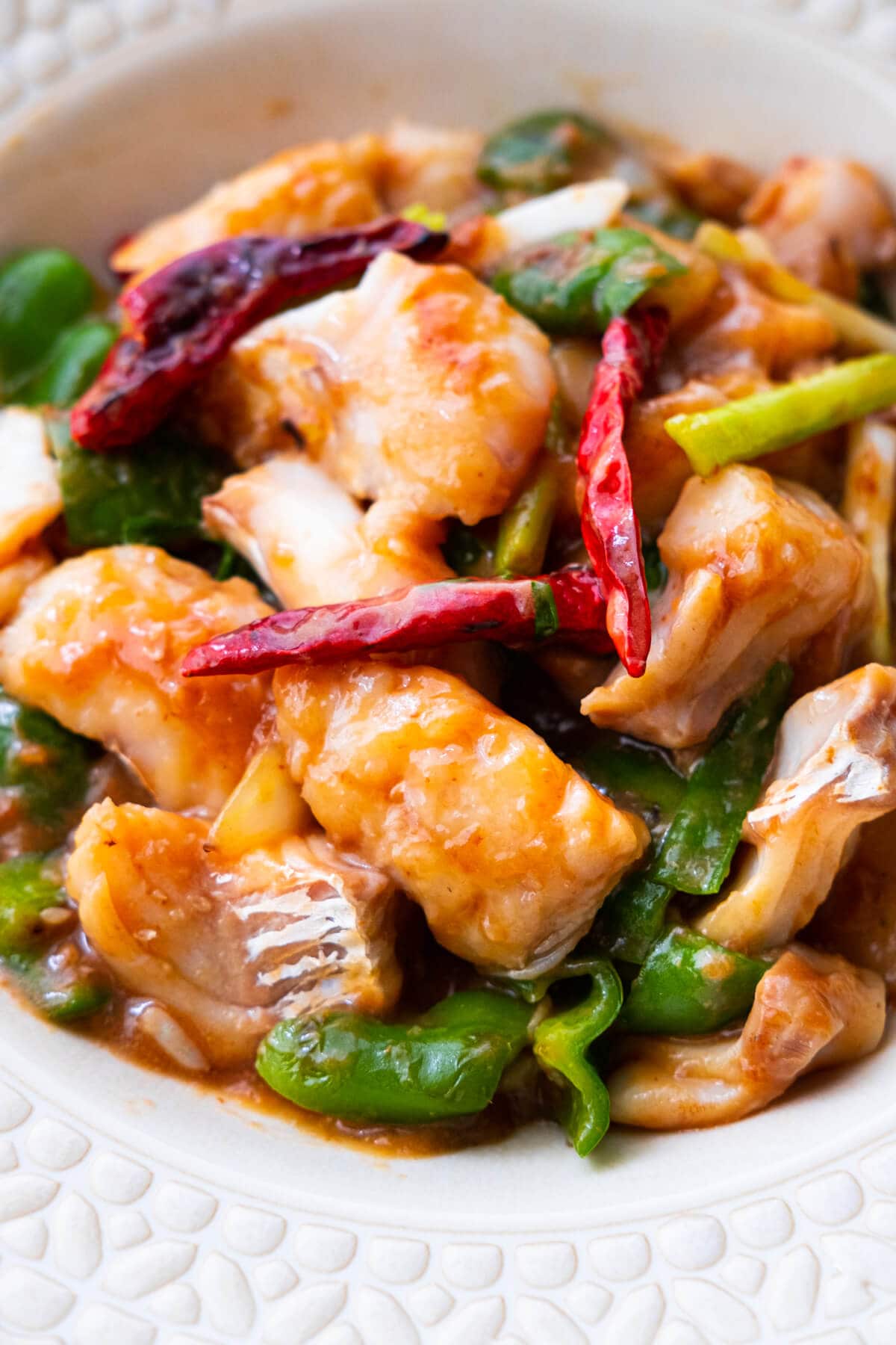 Stir-fried fish fillet with coated with black bean sauce, dried chilies, green bell pepper and onion, and served in a bowl. 
