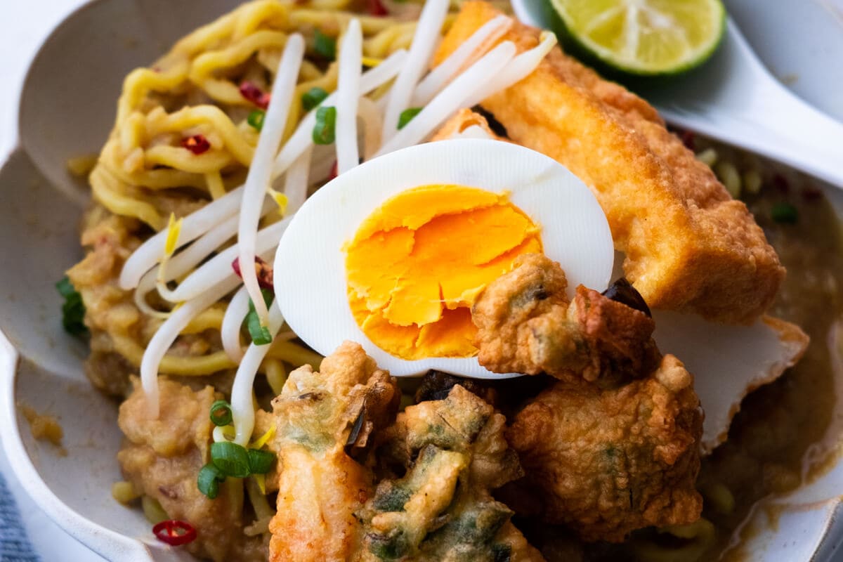 Serve the mee rebus in a bowl with beansprouts, hardboiled egg, prawn fritters, beancurd, lime and sambal. 