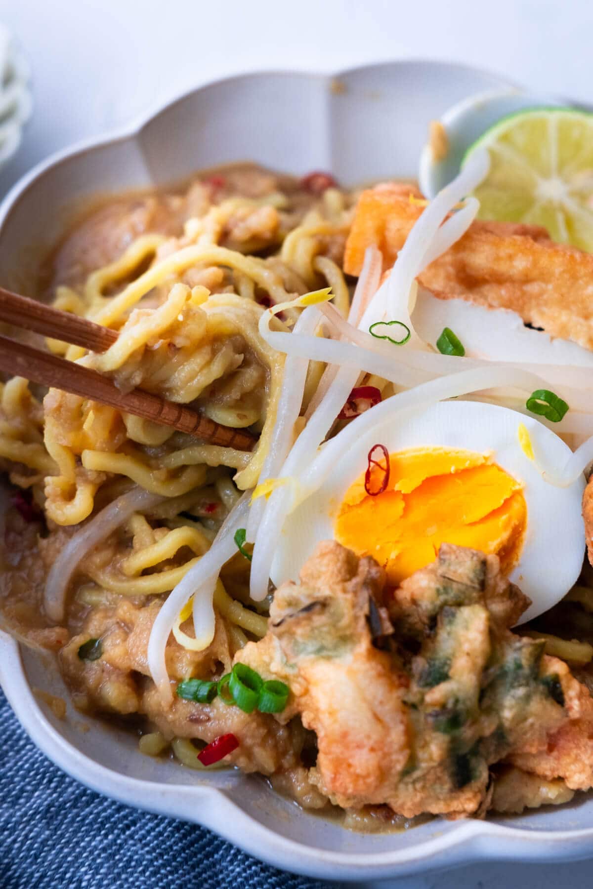 The yellow noodles are soaked in the gravy and the mee rebus is topped with hardboiled egg, prawn fritters, beansprouts, and lime. 