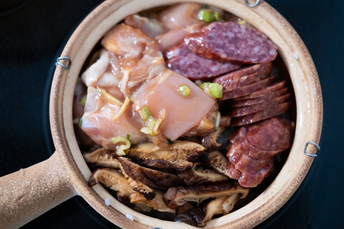 Marinated chicken, Chinese sausage, and shiitake mushrooms and rice in a claypot, ready to cook. 