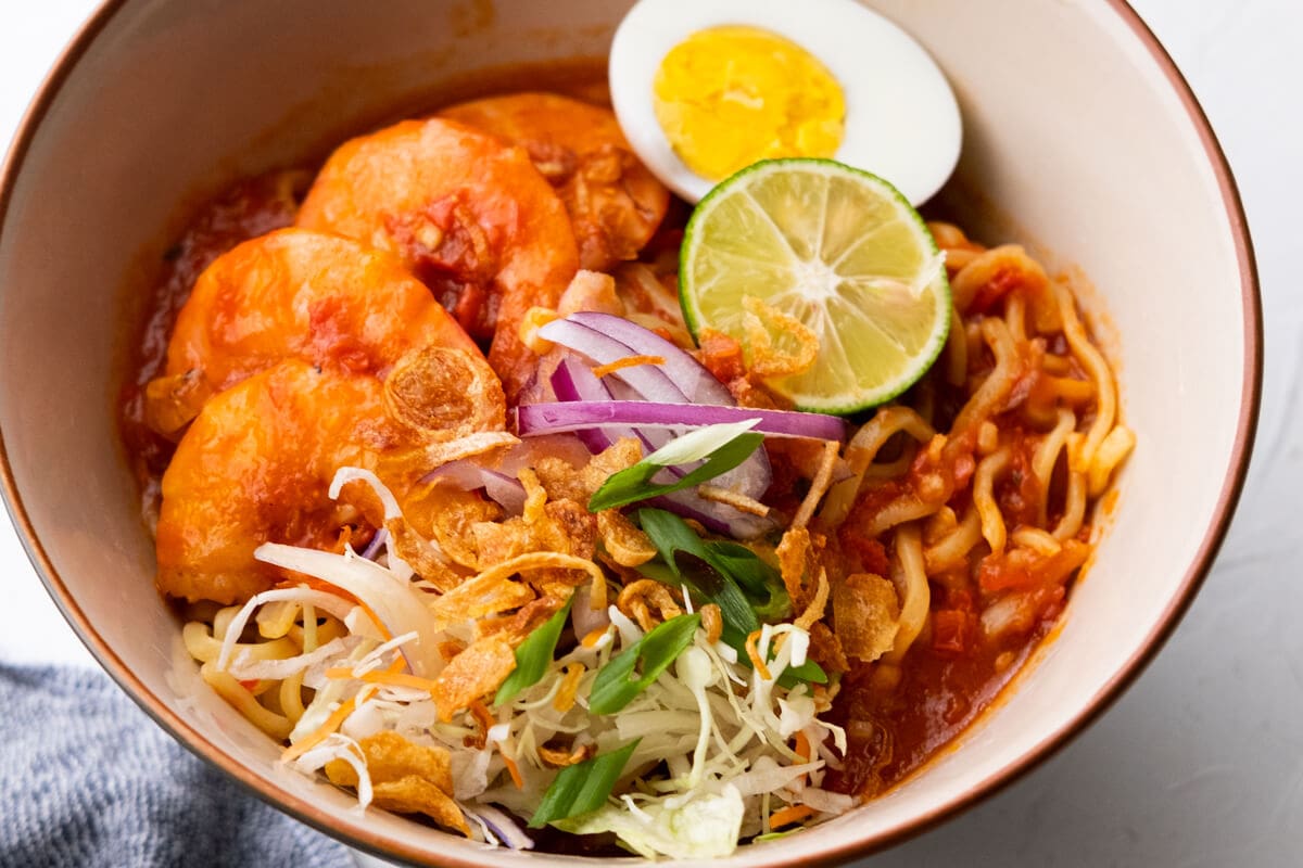 Garnish the malay prawn noodle with onion, spring onion, deep fried shallots, lettuce, egg and lime.  