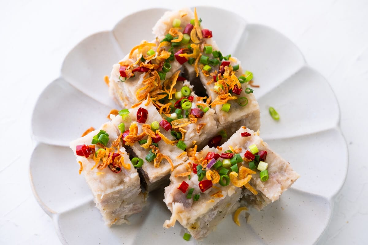 Slice the cooked yam cake into small slices, and top them with red chillies, dried shrimps, deep fried shallots, and spring onions. 