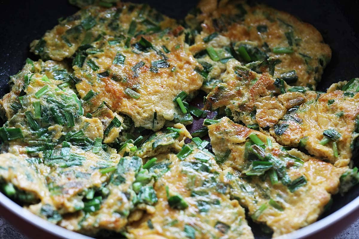 Chive omelet cut into pieces in a pan. 