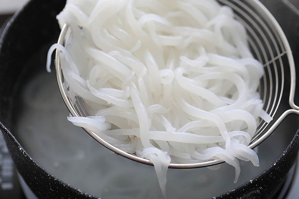 Draining boiled bee tai bak rice noodles using a colander.