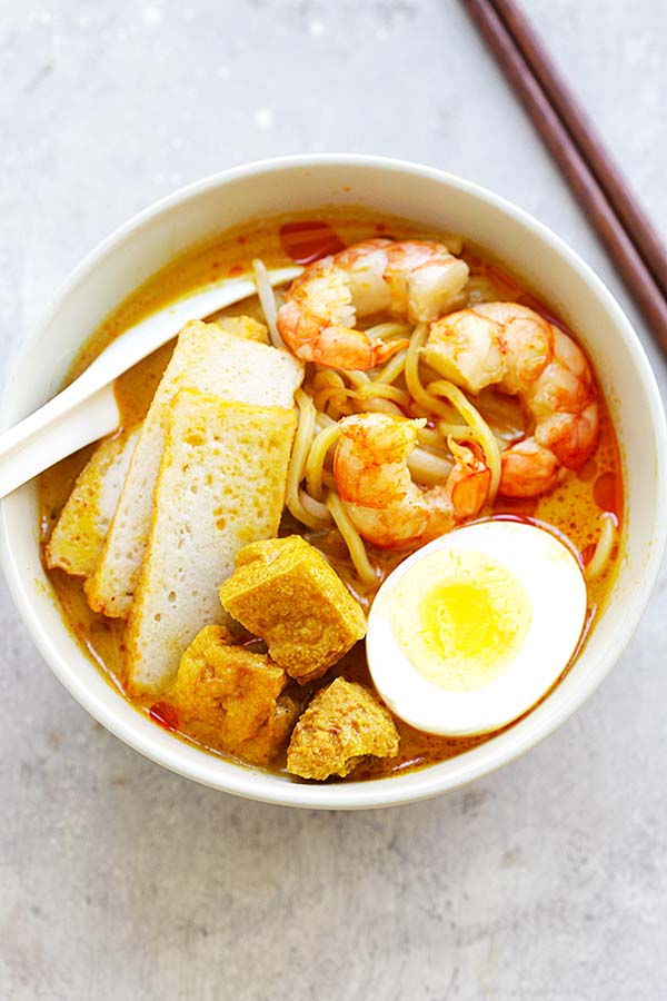 Spicy street food laksa noodle dish from Malaysia and Singapore, served in a bowl, topped with boiled eggs, tao pok, shrimps and sliced fish cakes.