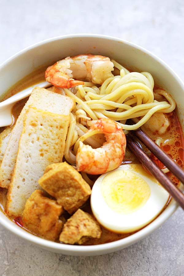 Curry Laksa in a bowl, with a pair of chopsticks picking the noodles.