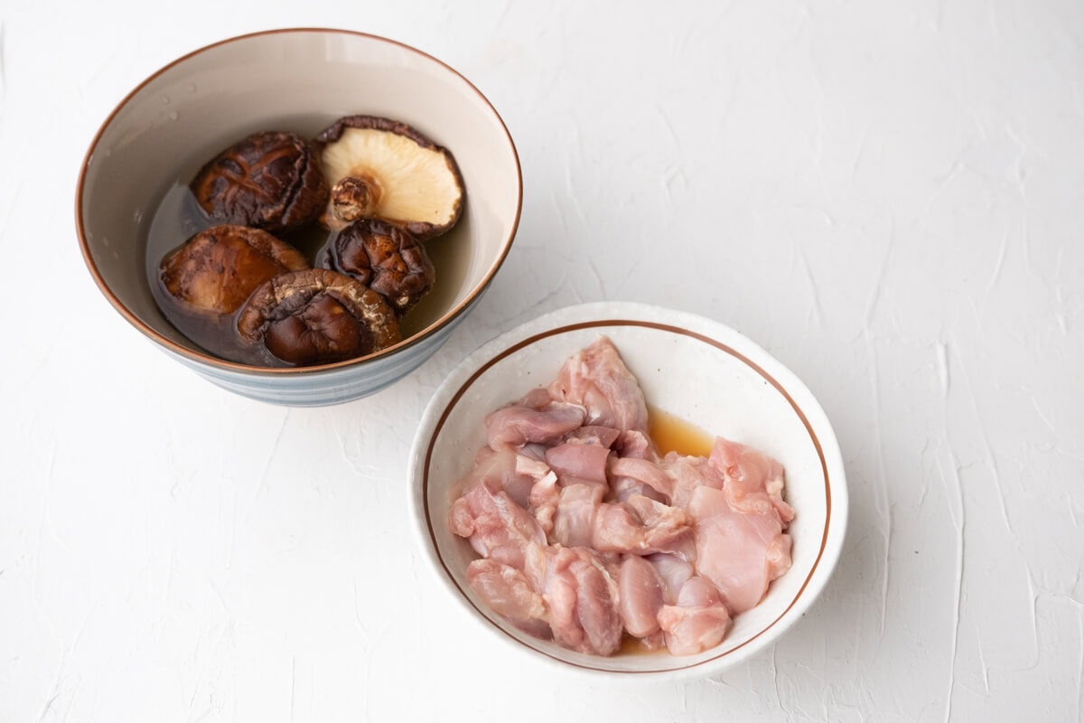 Shiitake mushrooms being soaked in water. Chicken thigh being marinated in a bowl. 