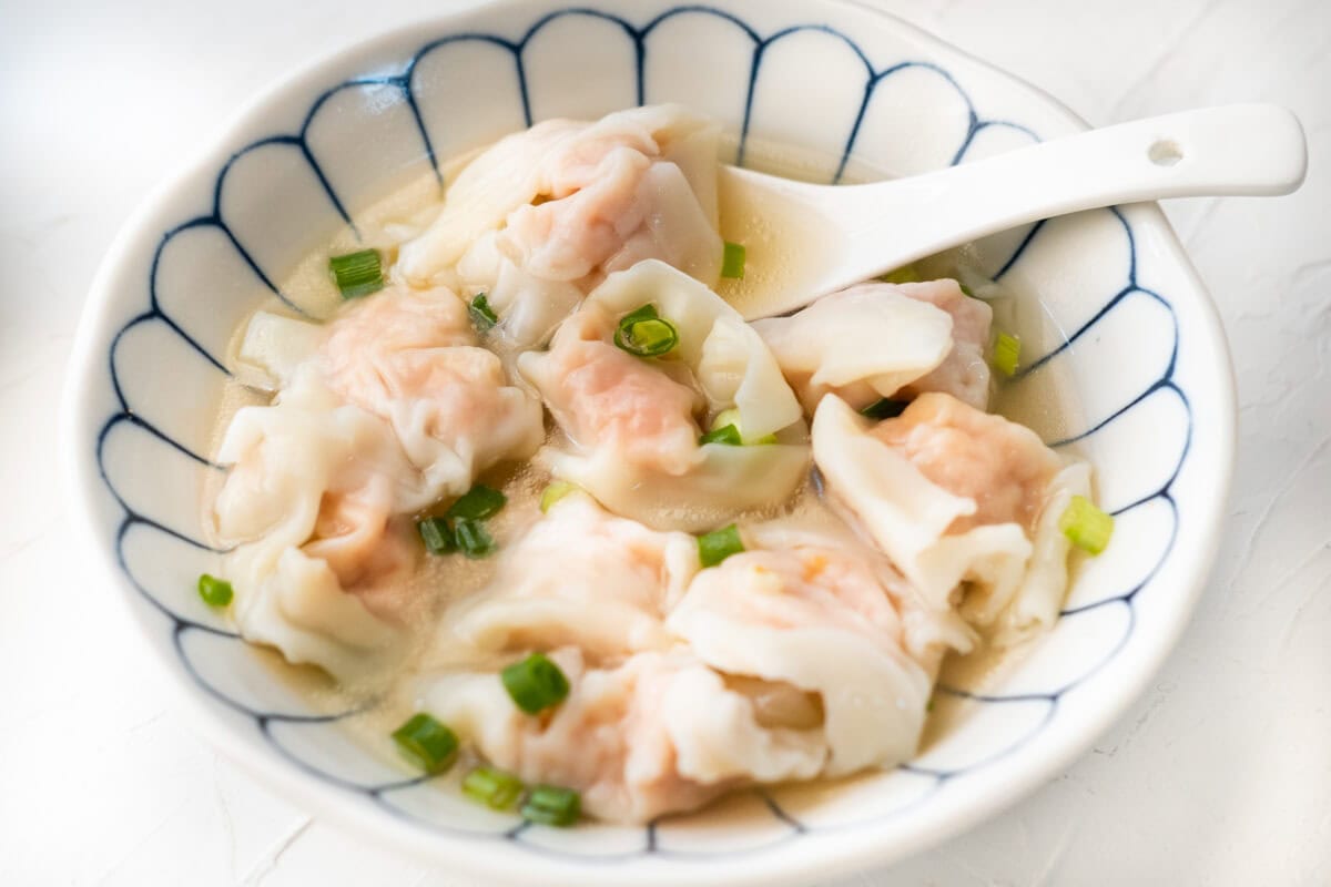 Cooked wontons in a small bowl and topped with chopped scallion. 