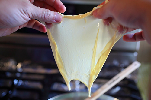 Hands holding tofu skin while waiting for excess soy milk to drip off.