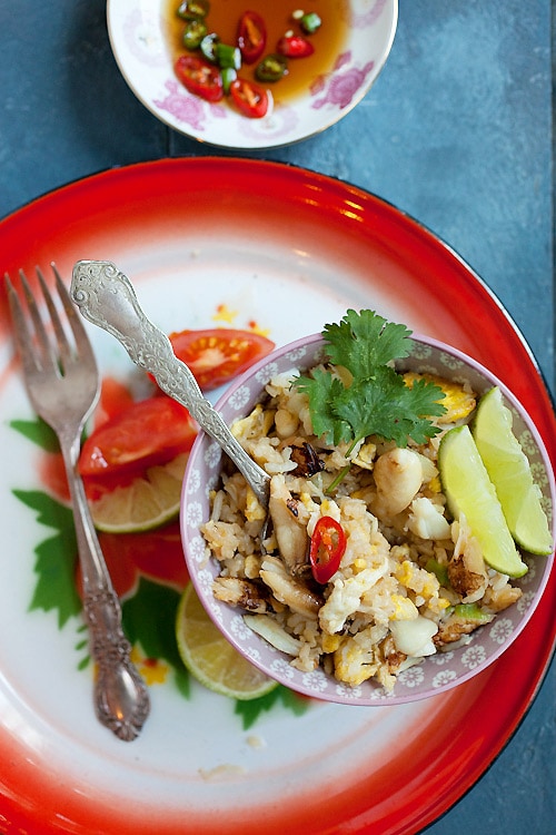 Easy and tasty Thai-style fried rice dish with rice, eggs, and crab meat with a side of sliced limes, and garnished with cilantro leaf.