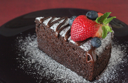 A piece of homemade no bake chocolate cake dusted with flour and decorated with berries.