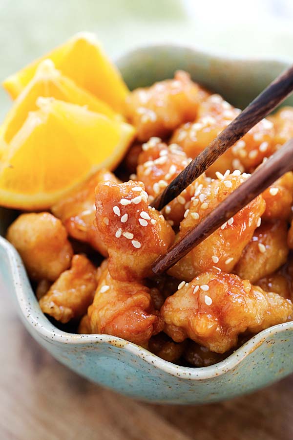 Deep-fried orange chicken in a yummy sauce being picked up by chopsticks.