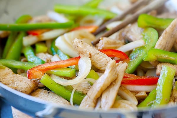 Black pepper chicken stir fry in a skillet with a pair of chopsticks in between.