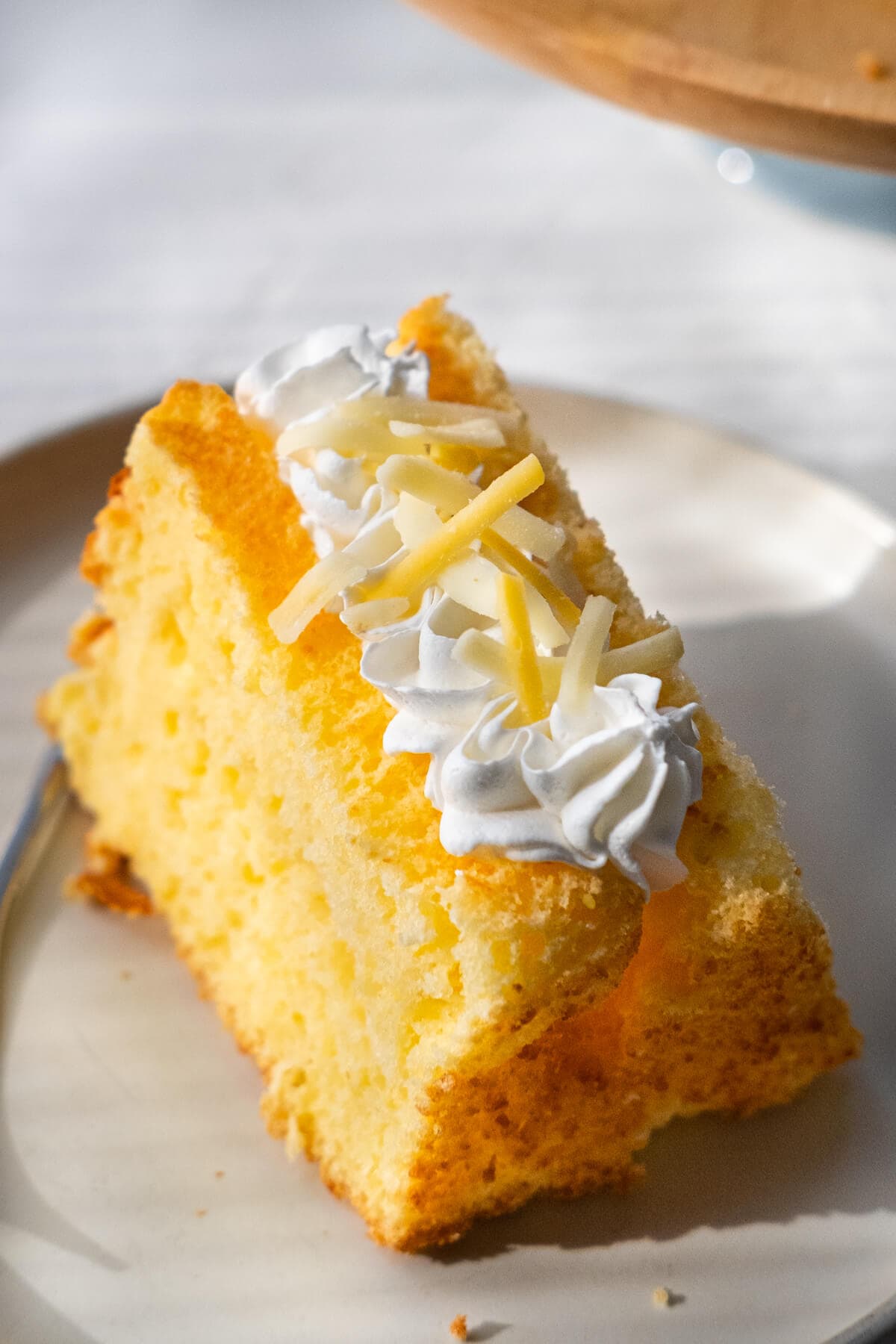 A slice of parmesan chiffon cake topped with whipped cream and shredded cheese.