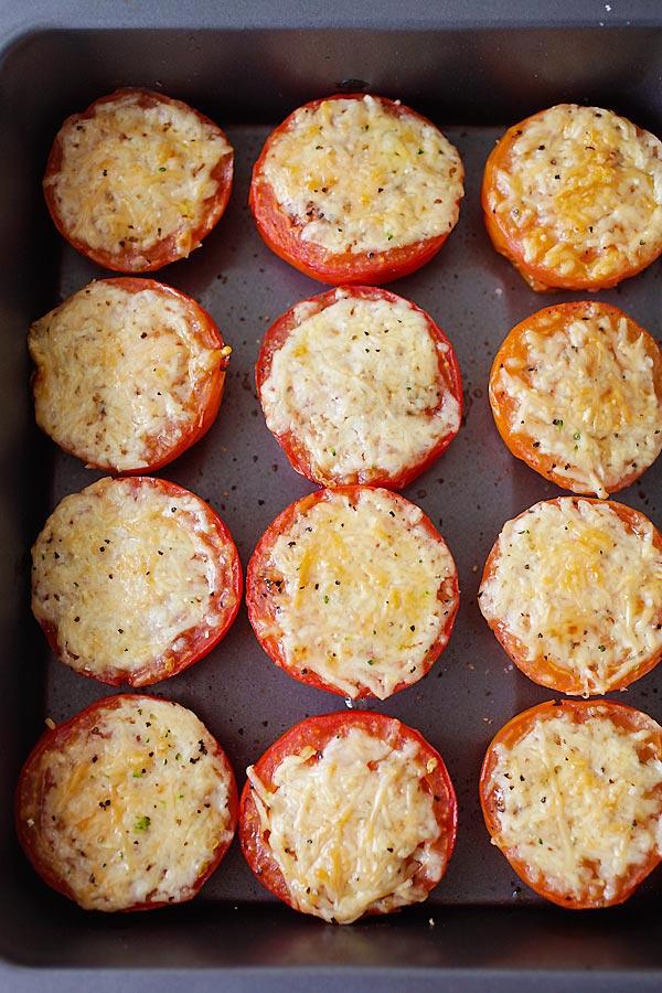 Juicy homemade oven roasted tomatoes with Parmesan cheese lined up side by side in a baking tray.