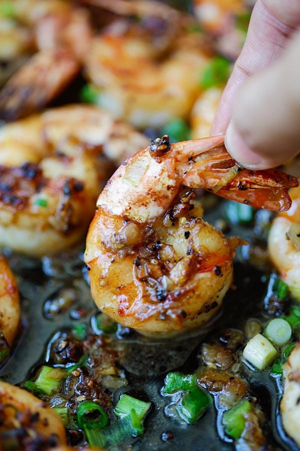 Close up garlic butter black pepper shrimp pinched in fingers.