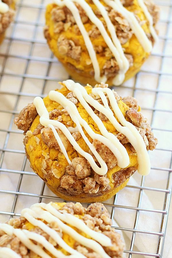 Pumpkin doughnut muffins topped with cream cheese icing over a sweetened crumble on cooling rack.