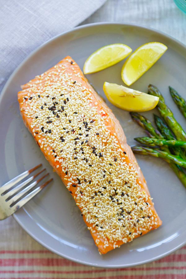 Healthy baked sesame salmon dish in a plate with asparagus and sliced lemon.