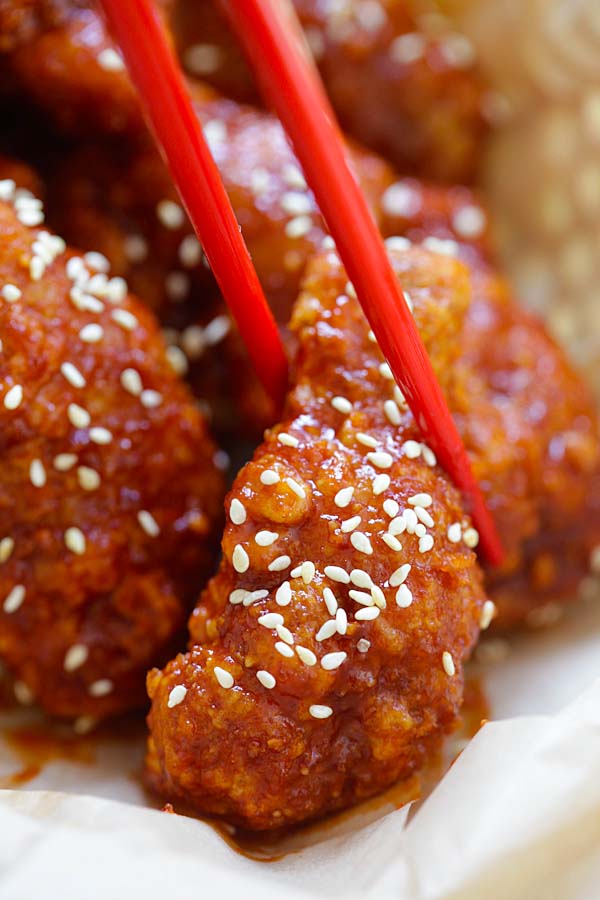 Red chopsticks picking up a piece of spicy-sweet Korean Fried Chicken.