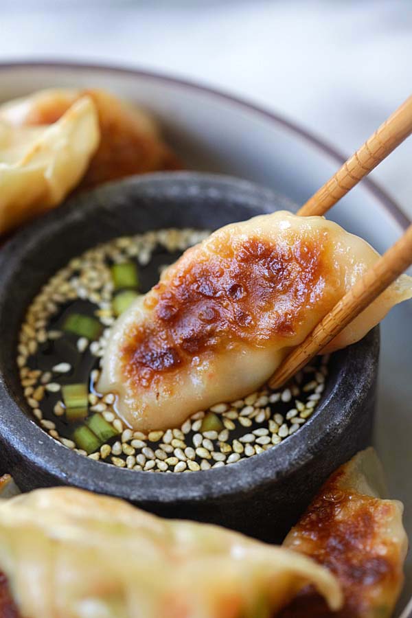 Homemade healthy shrimp gyoza dipped in gyoza dipping sauce with a pair of chopsticks.