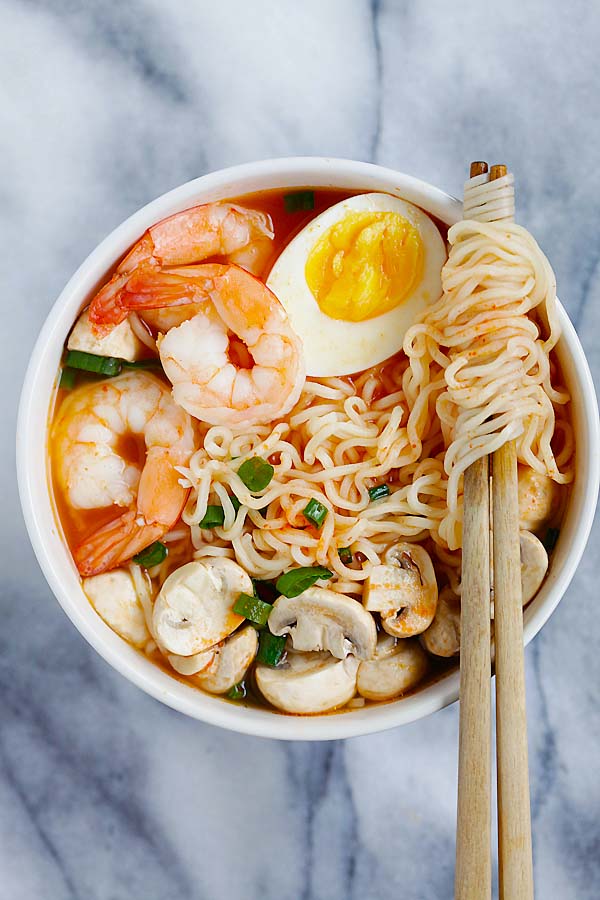 Easy and delicious sriracha ramen in a bowl with a pair of chopsticks picking so noodles.