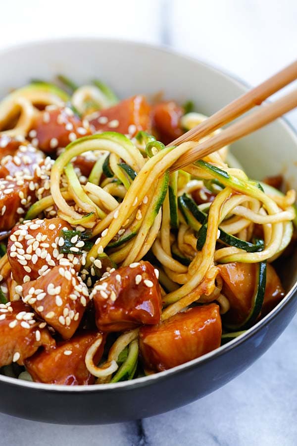 Easy healthy zoodles with sweet and spicy honey sriracha chicken, picked with a pair of chopsticks.