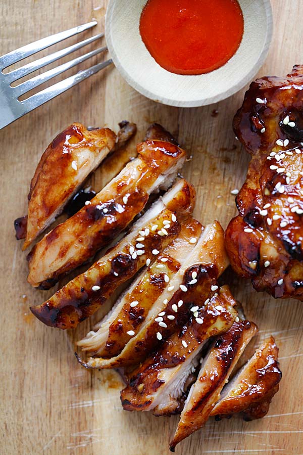 Sliced hoisin sriracha chicken on top of wooden chopping board.