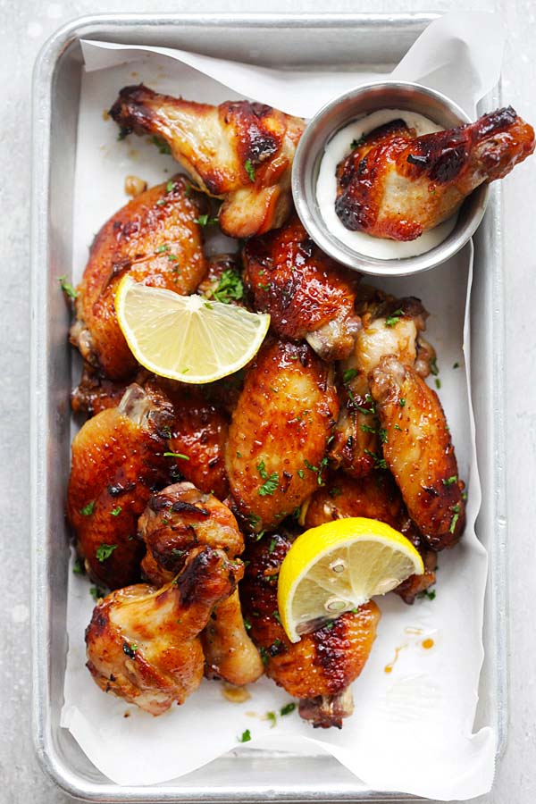 Baked to golden brown chicken wings with garlic lemon glaze, with a side of ranch dipping sauce in a baking tray.