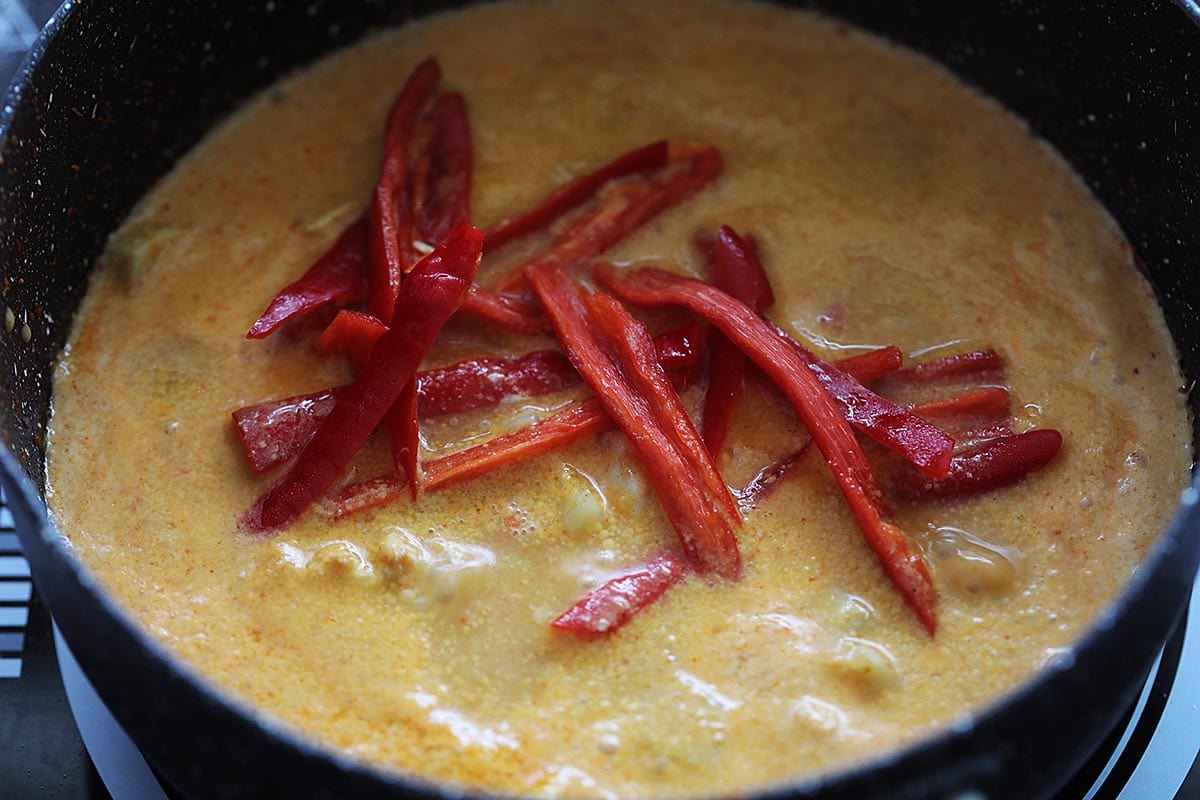 Adding red chilies to a pot of creamy  red Thai curry. 