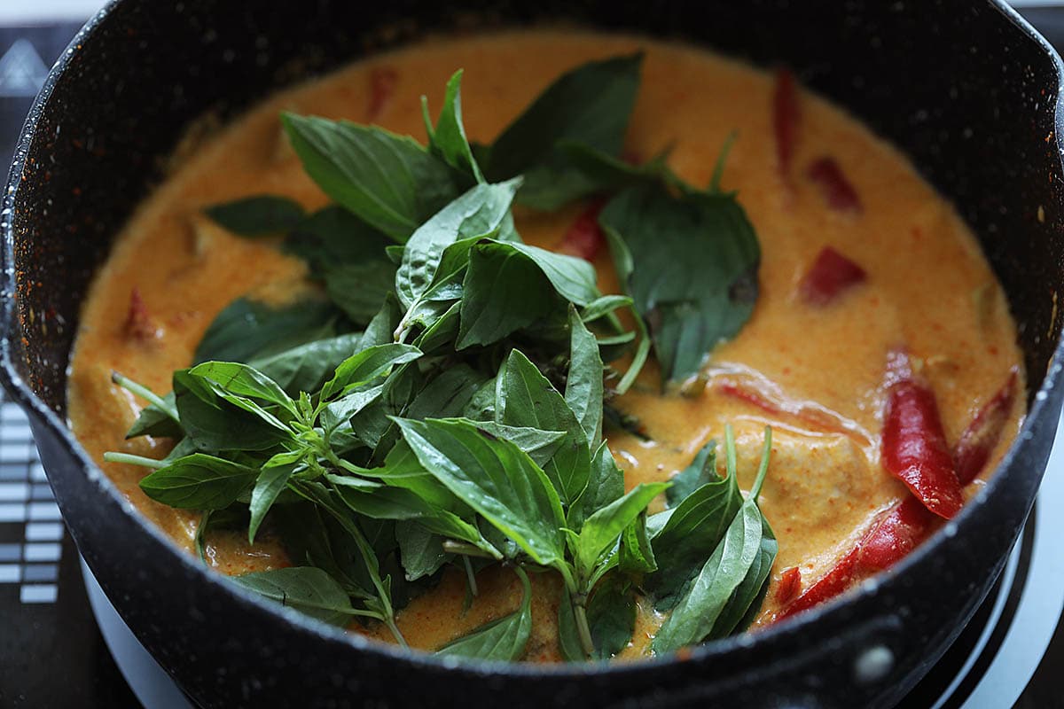 Adding Thai basil to red curry chicken in a pot. 