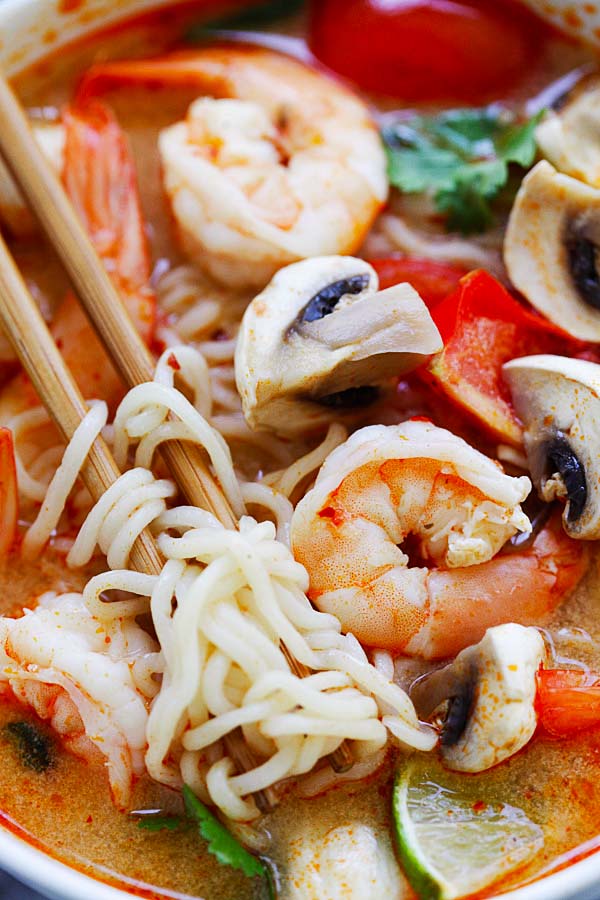 Close view of a pair of chopsticks picking some ramen noodles in a bowl of Thai Shrimp Noodle Soup.