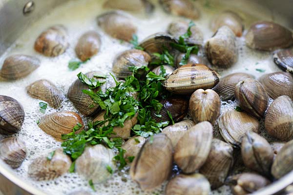 Making a steamed clams recipe in a skillet.