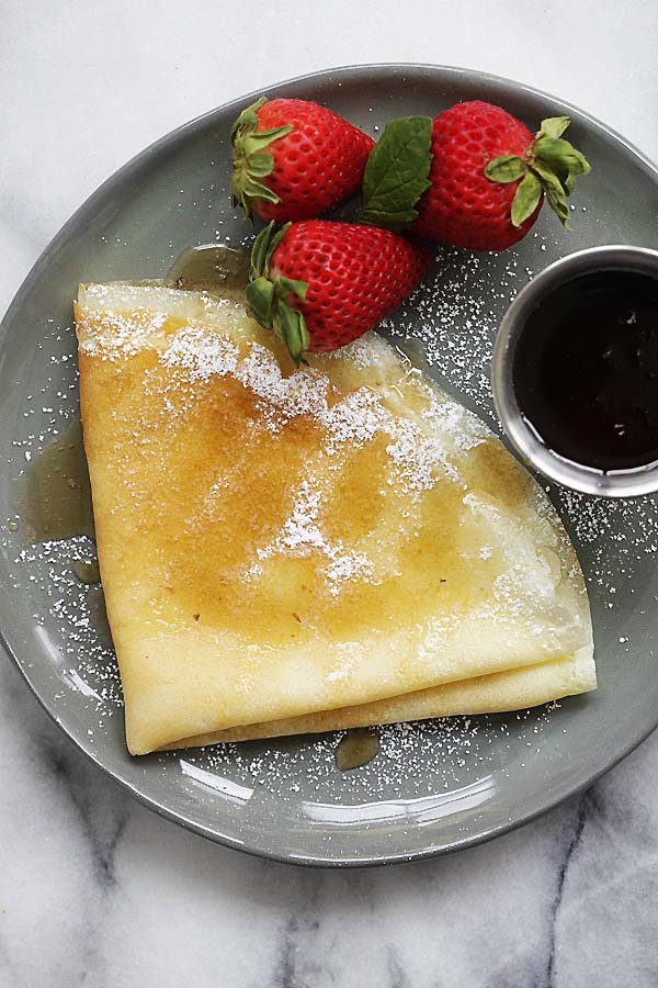 Crepe recipe with strawberries, melted butter, maple syrup and powdered sugar.