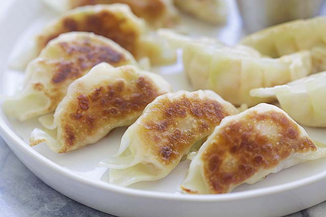 Golden pan-fried shrimp potstickers with a pair of chopsticks on a white plate.