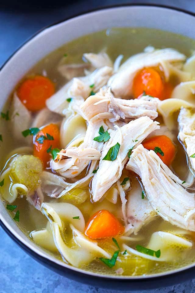 Close up shot of shredded chicken on top of chicken noodles soup, in a bowl.