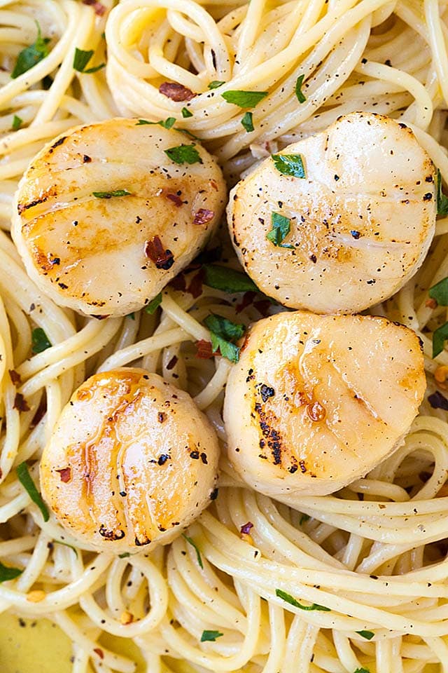 Macro shot of four big scallops on a bed of spaghetti aglio olio.