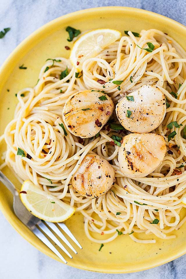 Creamy spaghetti, topped with scallops on a yellow plate, with a fork. 