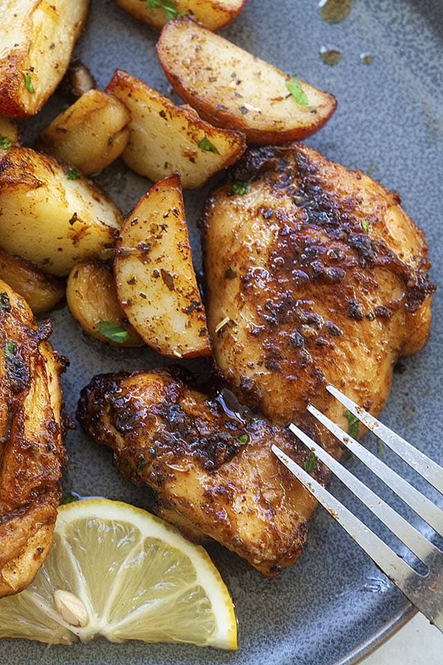 Skillet chicken thighs and potatoes with a fork, ready to be eaten.