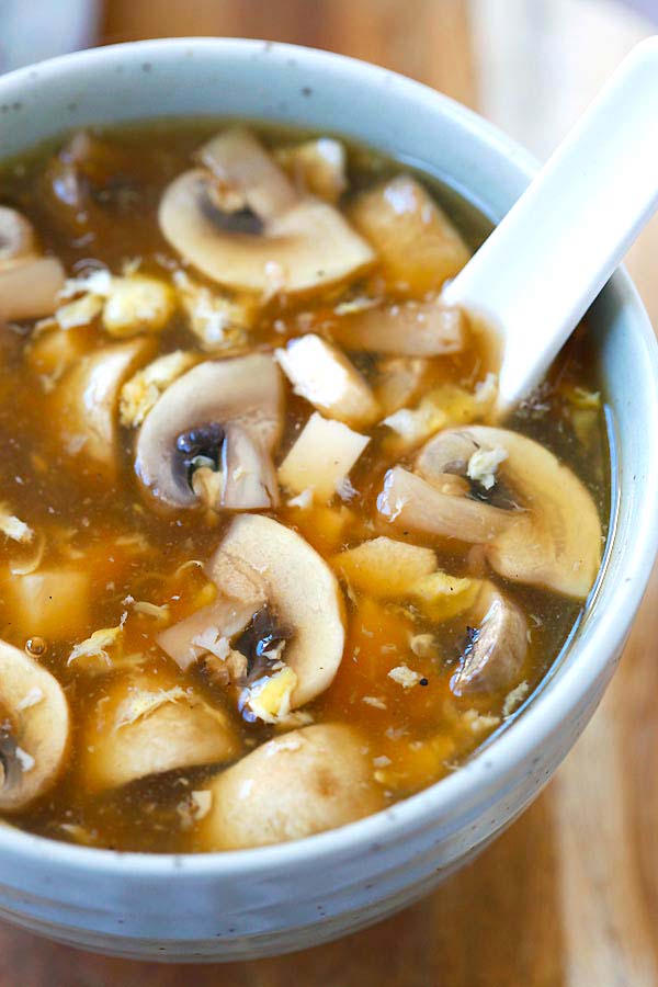 White button mushrooms and soft tofu in hot and sour soup served in a bowl with a spoon. 