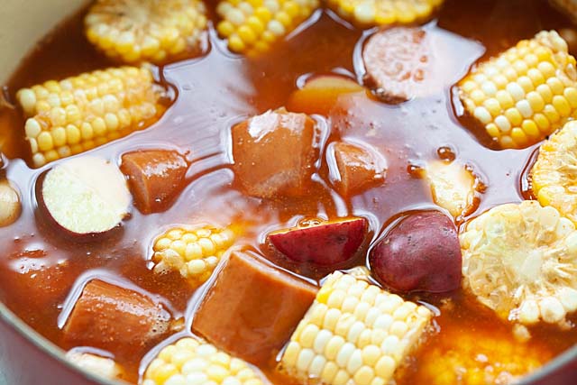 Adding corns, smoked sausages and red potatoes to a pot to make crawfish boil.