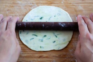 Rolling out a scallion pancake with a wooden rolling pin.