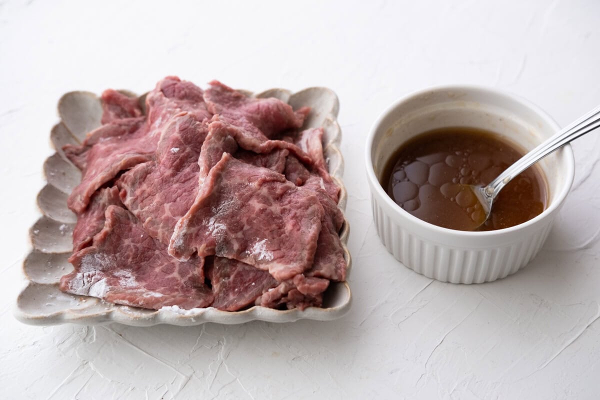 Ginger scallion sauce in a bowl and raw beef slices on a plate. 