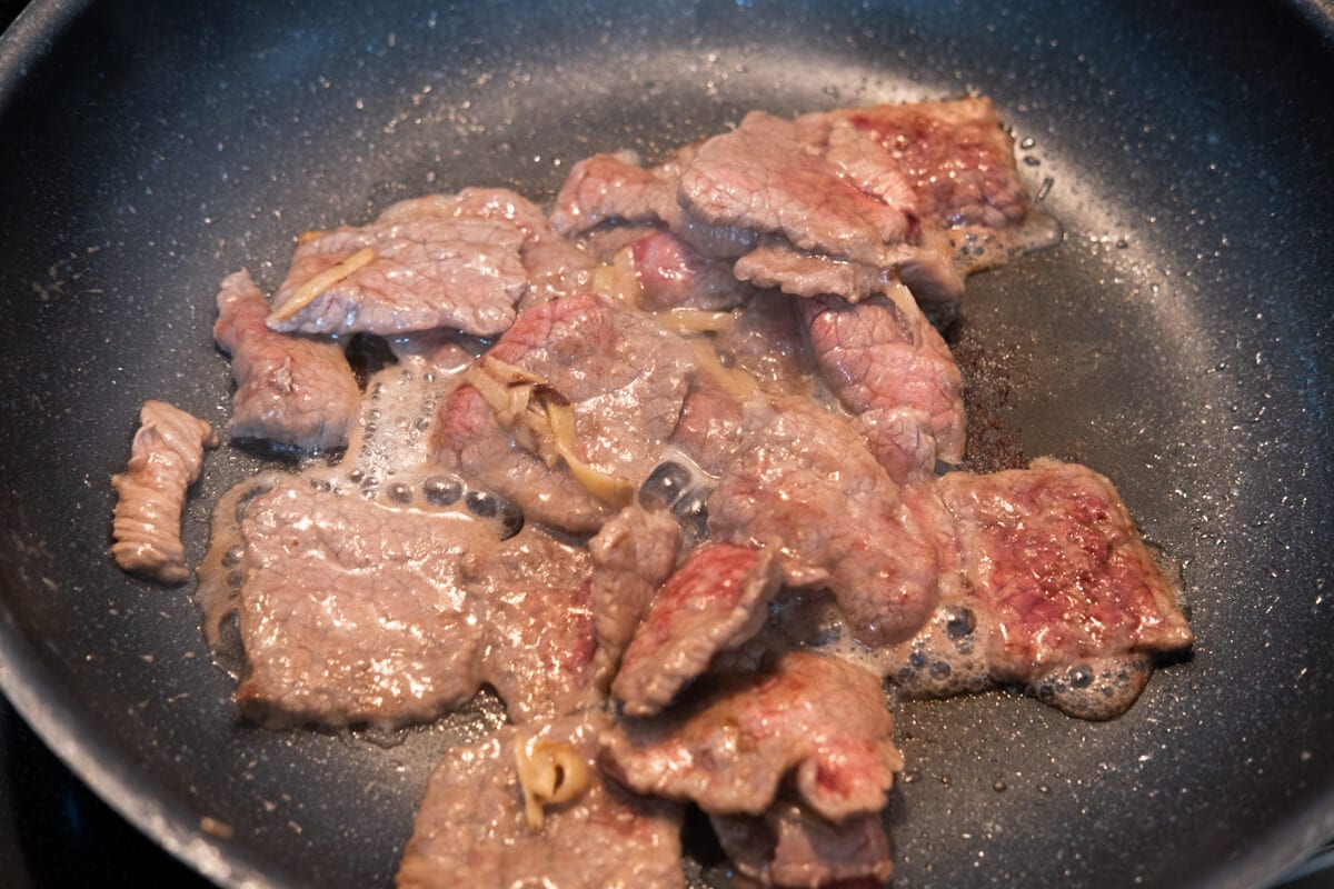 Stir frying beef with ginger and spring onions in a  wok. 