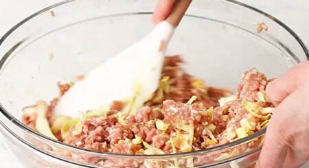 Mixing pork and vegetable filling in a bowl for lumpia rolls.