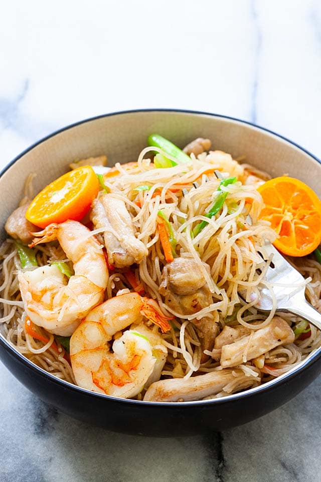 A fork picking up Filipino noodles or pancit in a bowl.