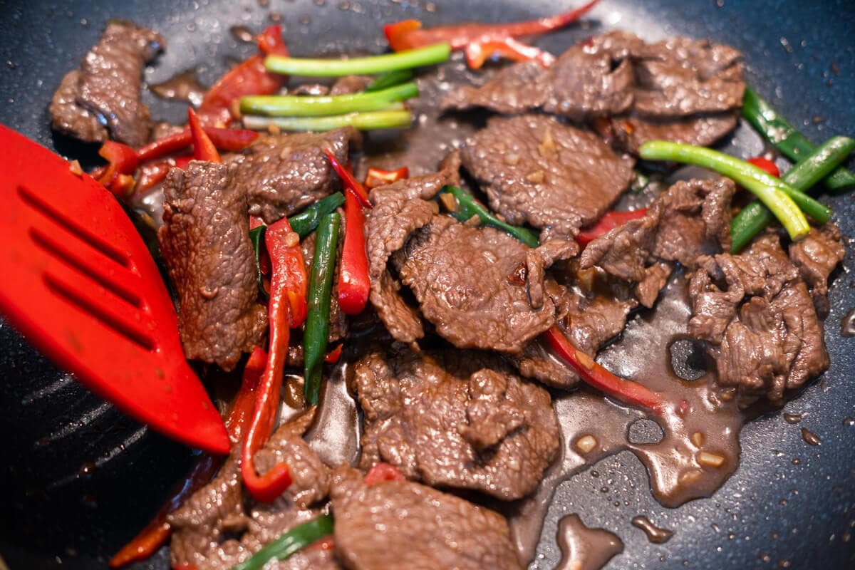 Stir frying flank steak beef slices with red bell pepper, chili flakes, and scallion in sesame sauce. 