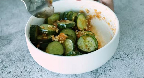 Tossing the cucumber slices with the Asian salad dressing.